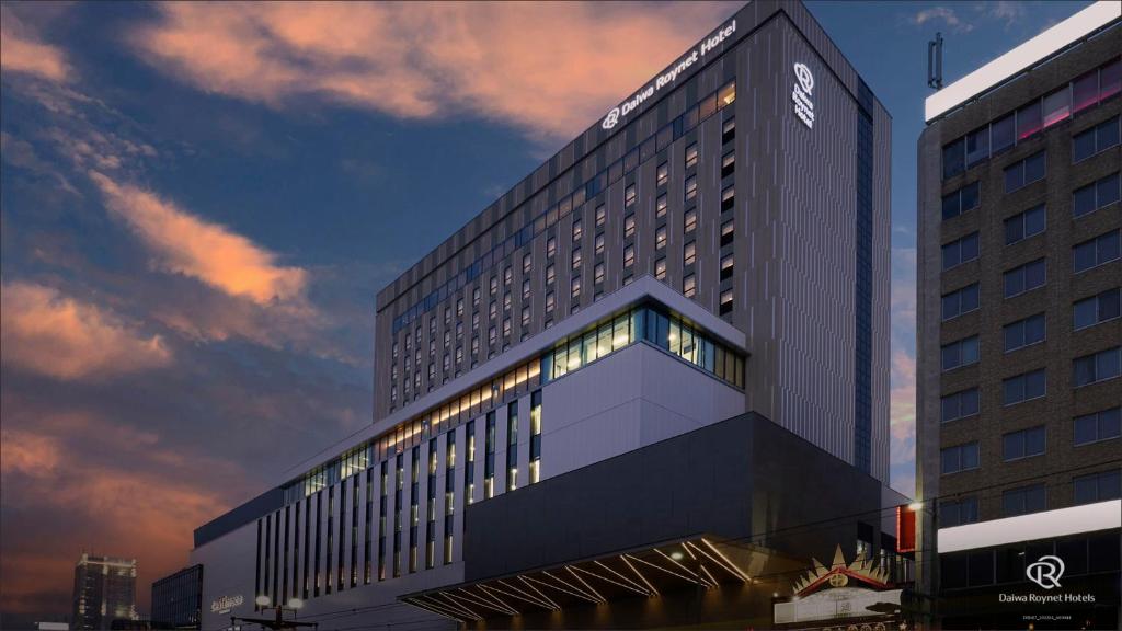 鹿儿岛Daiwa Roynet Hotel Kagoshima Tenmonkan PREMIER - former Daiwa Roynet Hotel Kagoshima Tenmonkan的一座高大的建筑,背面有日落