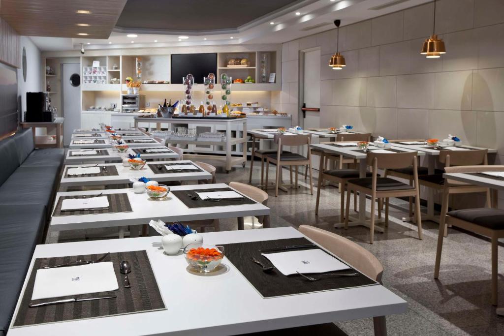 a restaurant with white tables and chairs and a kitchen at NH Madrid Atocha in Madrid