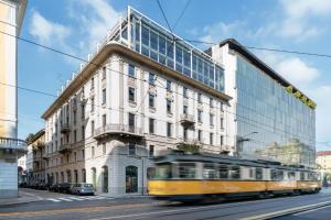 un treno giallo che passa davanti a un edificio alto di HOTIDAY Room Collection - Milano Cinque Giornate a Milano